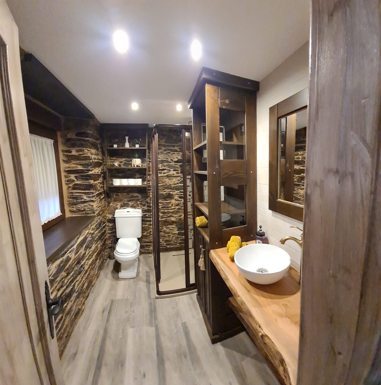 Baño rústico y moderno del Hotel Rural O Lar de Alba en Galicia, con paredes de piedra, ducha y lavabo contemporáneo.